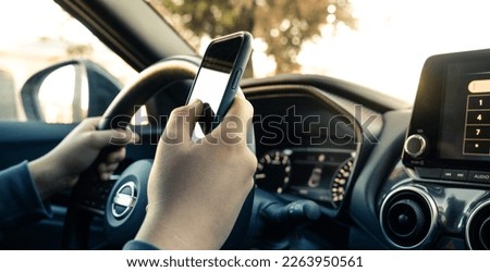 Teen drive a car and use smartphone. Young man reading messages holding a cell phone while driving. Dangerous behavior, accident risk. Danger, transgression, youth, distraction concept. Focus on hand.