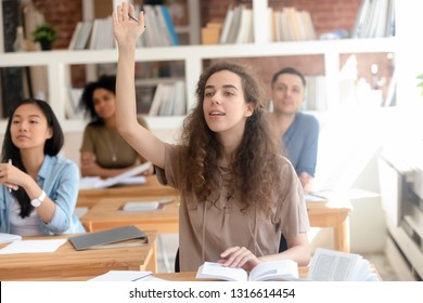 Teen Female College University Student Raising Hand During Class With Multinational Classmate Group, Smart High School Girl Asking Question At Lesson Sitting At Desk, Leadership And Knowledge Concept