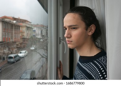 Teen in front of curtain watching the empty street from his window in anxiety
