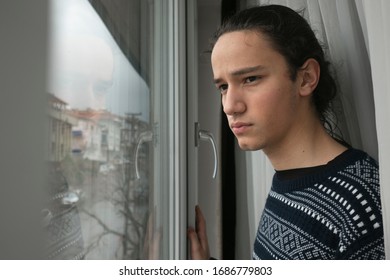 Teen in front of curtain watching the empty street from his window in anxiety