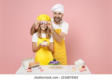 Teen fun girl dad father chef cook confectioner baker in yellow apron cap at table hold muffin covering eyes with macaroons isolated on pink background Mousse cake food workshop master class process