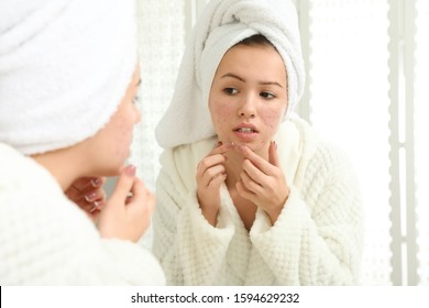 Teen Girl With Acne Problem Squeezing Pimple Near Mirror In Bathroom