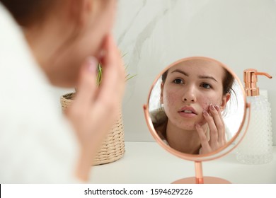 Teen girl applying acne healing patch using mirror indoors