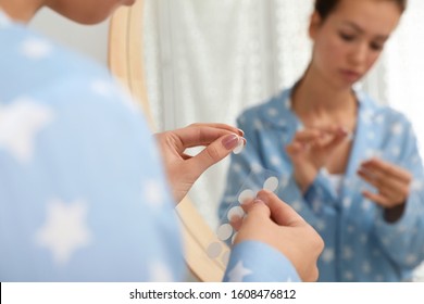 Teen girl applying acne healing patch near mirror in bathroom, focus on hands