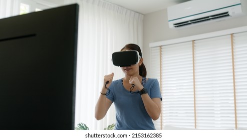 Teen girl asia enjoy play AR arcade game use hand punch motion in VR sport app online TV remote gym. Body fit fight class at home happy woman laugh in fun joy art youth culture with digital device.