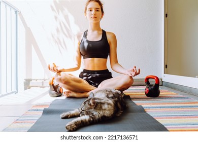 Teen girl attractive positive doing yoga sitting in Half Lotus exercise, Ardha Padmasana poses, workout, wearing sportswear, meditation session, indoor full length, home interior, cat near. doing spor - Powered by Shutterstock