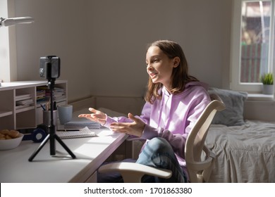 Una adolescente bloguera influenciante grabando el concepto de video blog hablando mirando el smartphone en trípode en la mesa de casa. Bloguero de medios sociales adolescente dispara vlog, transmitiendo podcast en línea por teléfono móvil.