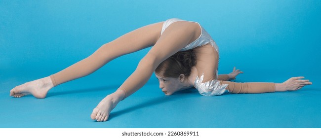 Teen Girl Contortionist Bent Over Backwards on the Floor Against a Blue Studio Background