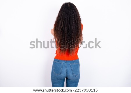 teen girl with curly hair wearing red sweater over white background hugging oneself happy and positive from backwards. Self love and self care.