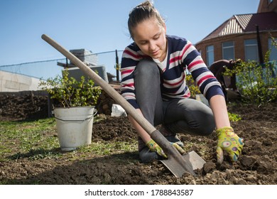 Teen girl dig a garden near a country house. Spring preparation for planting harvest concept. Help for parents at the infield.