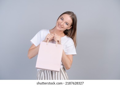 Teen girl doing shopping holding shopping bag in her hands fashion young woman shopper isolated on gray background. Beautiful happy girl in white light clothes. Copy space and mock up. Seasonal