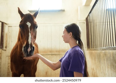 Teen girl dressed in a bright purple shirt is happily feeding a beautiful brown horse, creating a warm and joyful scene between them - Powered by Shutterstock