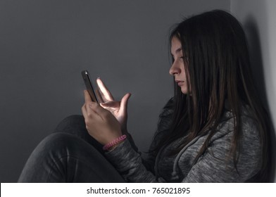 Teen Girl Excessively Sitting At The Phone At Home. He Is A Victim Of Online  Social Networks. Sad Teen Checking Phone Sitting On The Floor In The Living Room At Home With A Dark Background. 