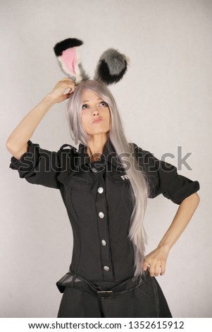 teen girl in FBI black carnival dress with big fur rabbit ears loves cosplay and stands on white Studio background