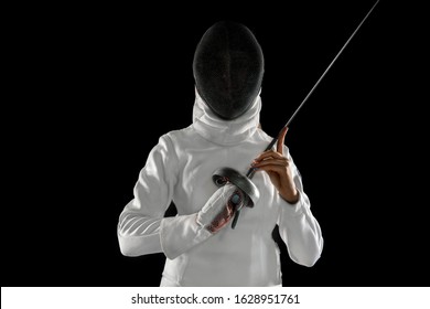 Teen girl in fencing costume with sword in hand isolated on black background. Young female model practicing and training in motion, action. Copyspace. Sport, youth, healthy lifestyle. Close up.
