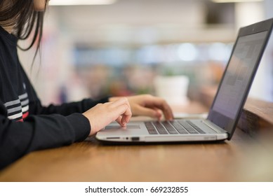 Teen Girl Hands Typing Laptop On Wooden Table With Blur Background.Young Woman Hands Typing On Laptop's Keyboard In Cafe.