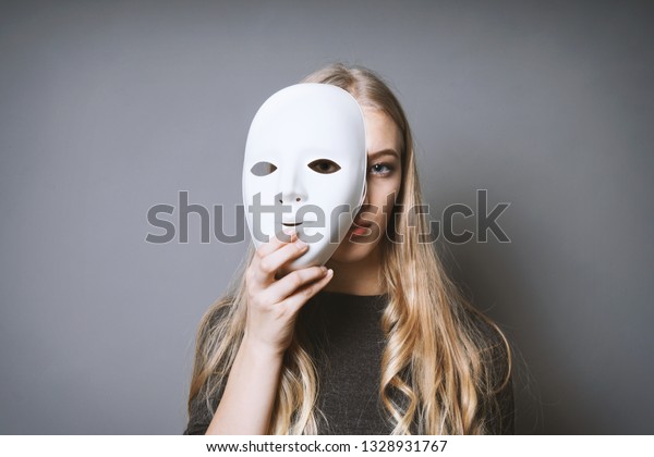 teen girl hiding her face behind mask - identity\
or personality concept