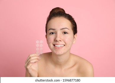 Teen girl holding acne healing patches on light pink background