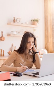 Teen Girl With Laptop Doing Homework In Bright Kitchen. Education And Business Concept. Remote Work And Freelance Work. Student. Vertical Photo