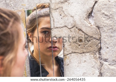 Teen girl looking at her reflection in the mirror fragments on the wall at street. 