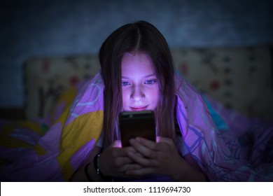 Teen girl lying in bed at night and looking at the glowing screen of smartphone. - Shutterstock ID 1119694730