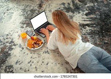 Teen Girl Lying On Floor With Blank Screen Laptop And Sweets Watching TV Series. Photography For Ad Or Blog