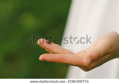 Teen girl on the background of a green field looking at a ladybug on her finger