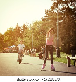 Teen girl on roller skates smiling and little boy bike on bicycle behind. Toned.