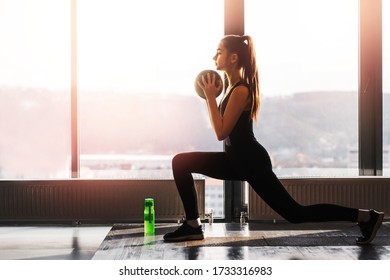 Teen Girl Performs A Warm-up With A Medicine Ball. Modern Stylish Gym With Large Panoramic Windows With Sunlight. Healthy And Active Lifestyle.