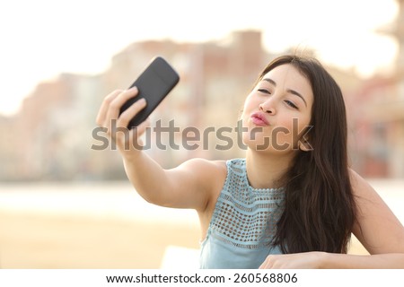 Teen girl photographing a selfie kissing camera with a smart phone in an urban park