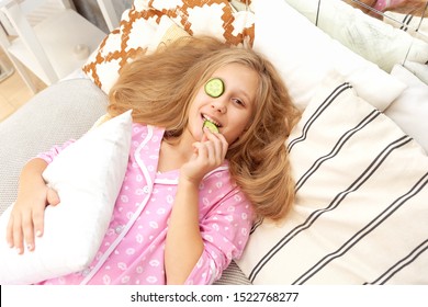 Teen girl in pink pajamas makes an eye mask from cucumber circles - Shutterstock ID 1522768277