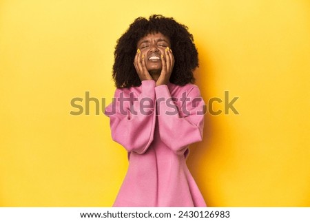 Teen girl in pink sweatshirt, yellow studio backdrop whining and crying disconsolately.