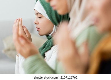 Teen girl praying near blurred women at home