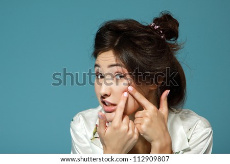 Teen girl with problem skin look at pimple. Morning theme. Over blue background.