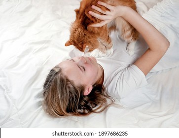 Teen girl relaxing in the bed with her cat, close-up. Friendship between kids and animals.