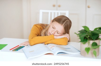 A teen girl rests her head on her arms while napping at a white table. She is resting on an open textbook with colored pencils lying beside it. - Powered by Shutterstock