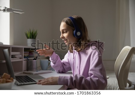 Teen girl school pupil wears headphones conference calling studying online with remote tutor from home. Teenage student using laptop talking in webcam video chat learning lesson with distance teacher.