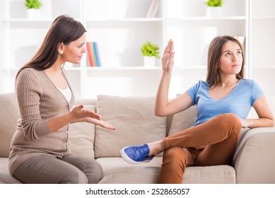 Teen Girl Is Showing Stop Gesture To Angry Mother While Sitting On Sofa At Home.