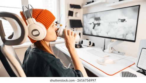 Teen girl sits in ergonomic chair and sips warm drink while taking a digital break. Minimalistic gaming setup with daylight window and soft vibes promotes calmness and comfort.