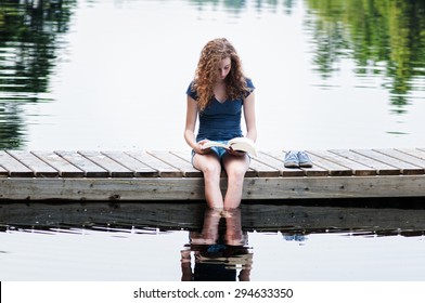 Teen Girl Sitting On A Dock Reading A Book