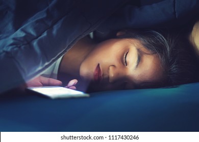 Teen Girl Sleeping In Bed With Smart Phone Under Blanket In Dark