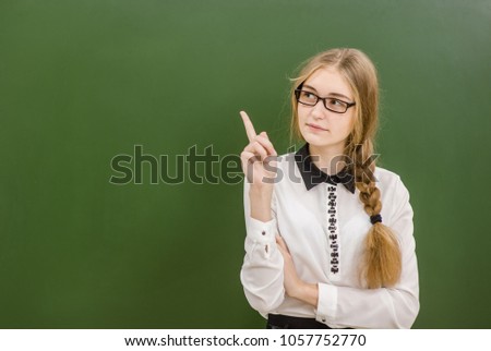 Teen girl standing near green chalkboard and pointing on empty space