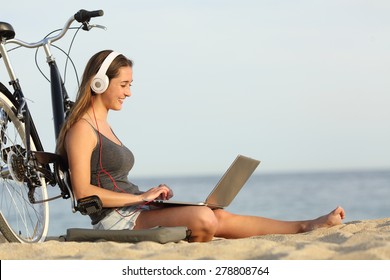 Teen girl studying with a laptop on the beach leaning on a bicycle