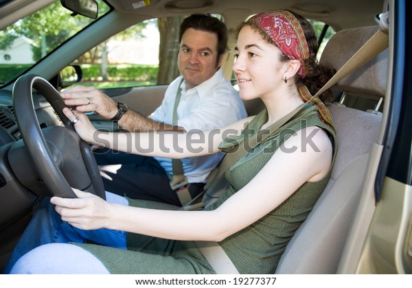 Teen girl taking driving lessons from an\
instructor or her father.