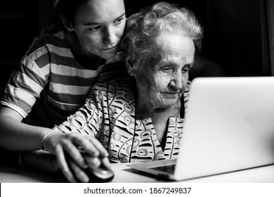 Teen Girl Teaches Her Grandmother To Work On The Computer Laptop. Black And White Photo.