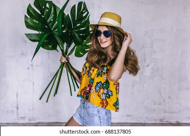 teen girl with tropical leaves in sunglasses and summer hat, summertime teen fashion