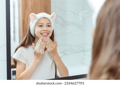 Teen girl washes her face with natural soap scrub cosmetic foam in bathroom portrait reflection in mirror. Teenage girl blonde do self care morning routine. Skin care cosmetic, lifestyle - Powered by Shutterstock