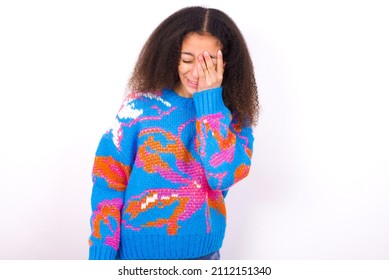 Teen Girl Wearing Colourful Knitted Sweater Against White Makes Face Palm And Smiles Broadly, Giggles Positively Hears Funny Joke Poses