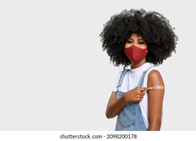  teen girl wearing face shield, points to the vaccineband aid on the square, you can see the smile in her eyes, isolated on gray background, covid-19