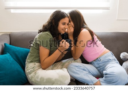 Teen girl whispering a secret to her happy best friend while drinking tea and talking about gossip